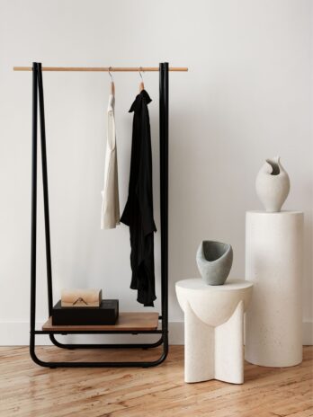 A minimalist retail display featuring a simple black clothing rack with garments hanging next to clean, geometric white ceramic pedestals holding small decorative items.