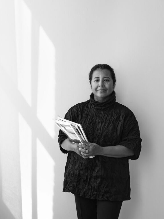 Black and white portrait of Claudia, co-founder of If Walls Can Talk, smiling and holding design magazines.