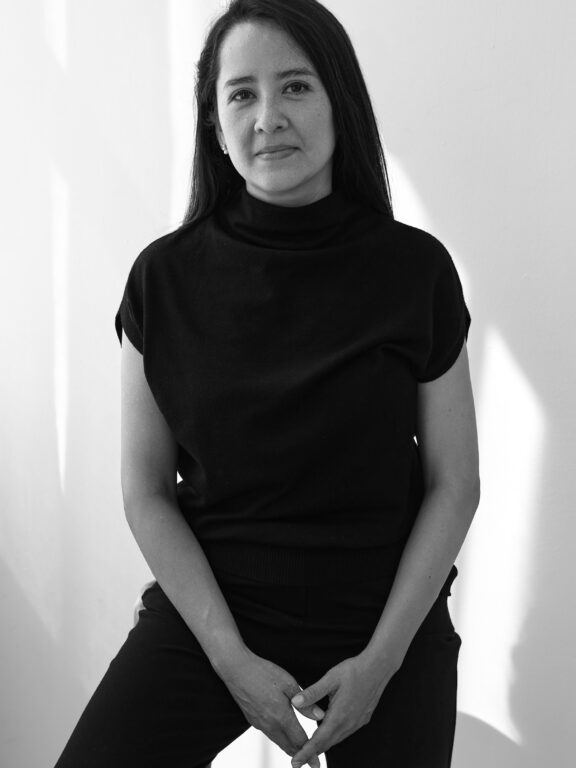 Black and white studio portrait of Marisol, co-founder of If Walls Can Talk, wearing a dark turtleneck.