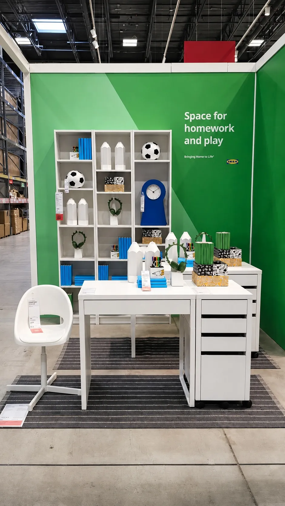 A display shows a study area with a white desk, white chair, and shelving unit with books, decorative items, a blue clock, and soccer balls against a green wall labeled Space for homework and play.