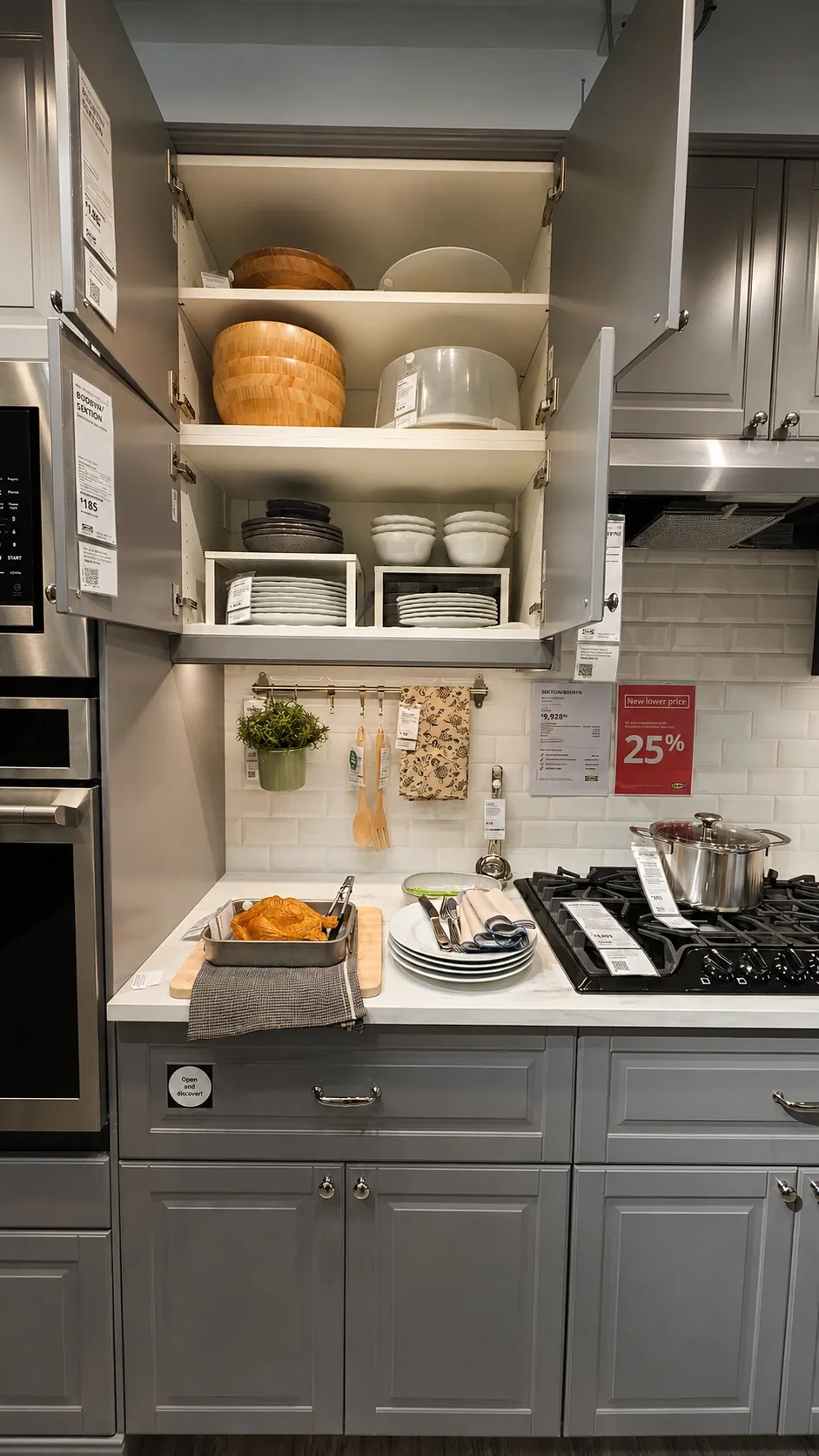 Modern kitchen with gray cabinets, open upper cupboards displaying neatly stacked dishes and bowls, a countertop with a roasted chicken on a cutting board, plates, utensils, and a pot cooking on the stove.