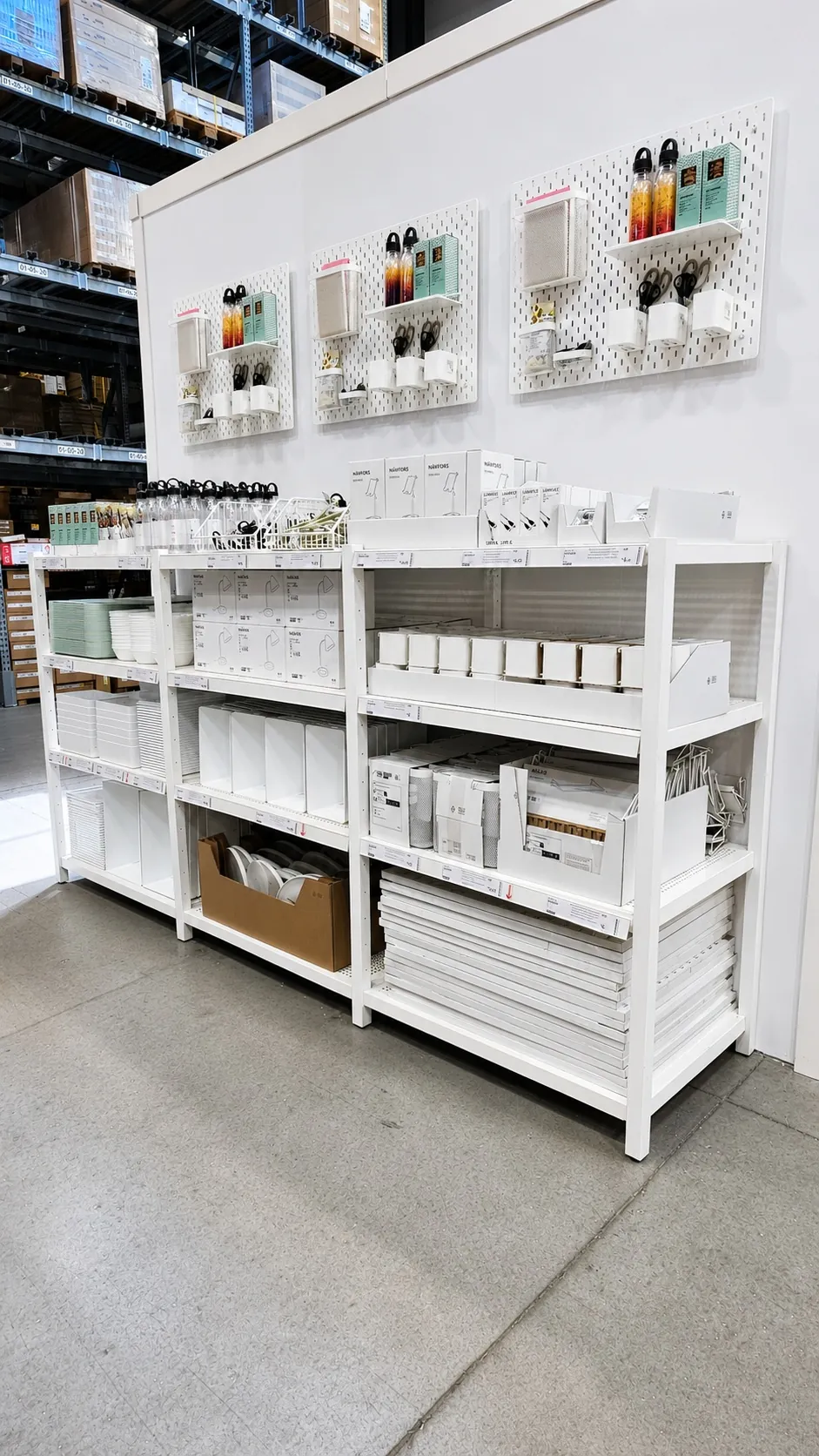 Shelves in a store display various white and neatly organized storage boxes and containers. Three pegboards above hold additional small organizing items. The setting appears clean and well-lit.